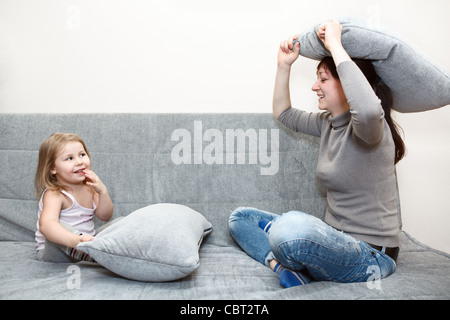 Kleine Kinder und junge Mutter in kämpfen auf dem Sofa Kissen. Lustige und fröhliche Freizeit. Stockfoto