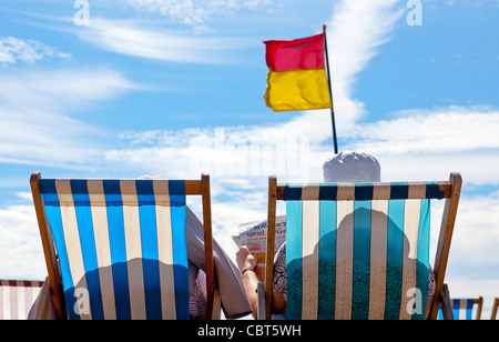 Zwei pensionierte und ältere Frauen sitzen auf Liegestühlen und entspannen sich am Meeresstrand. Stockfoto