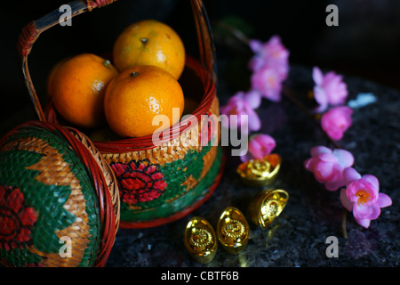 Korb mit Äpfeln und Orangen mit Goldbarren und Pflaumenblüte Stockfoto