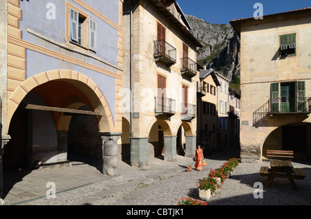 Woman Walking Dog & Street Scene with Arcades, Village Houses and Town Square, La Brigue, Roya Valley, Alpes-Maritimes, France Stockfoto