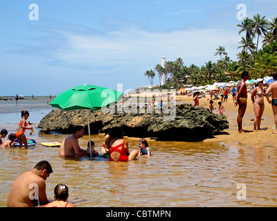 Familien, Baden und genießen Sie den schönen Strand von Praia Forte, Brasilien, mit Palmen und dem Leuchtturm im Hintergrund Stockfoto