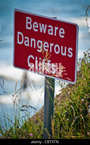 Passen Sie auf das Schild „Dangerous Cliffs“ am Rand einer steilen Klippe mit dem Meer unten auf Stockfoto