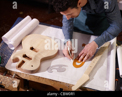 Mitte erwachsener Mann bei der Arbeit als Handwerker in italienischen Werkstatt mit Gitarren und Baupläne Skizzen. Erhöhte Ansicht Stockfoto