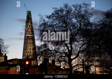 Die Scherbe im Bau in der Nacht sitzt hinter der Silhouette eines riesigen Baumes. Die Scherbe (aka The Shard of Glass) wird auf der Südseite der Stadt in der Nähe von London Bridge gebaut. Shard London Bridge, früher bekannt als London Bridge Tower, und auch der Shard of Glass. Stockfoto