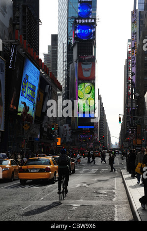 Sonnigen Porträt Radfahrer gelben taxis, 7th Avenue bei West 46th Street in Richtung Grün Blau Neon Times Tower Straßenschlucht, New York Stockfoto