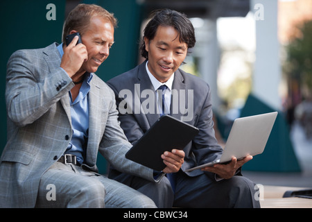Geschäftsleute, die mit Laptop und Tablet pc, während Kommunikation auf Handy Stockfoto