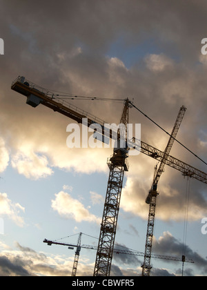 Baukräne, die vor Sonnenuntergang mit sichtbaren Wolken im Hintergrund stehen Stockfoto