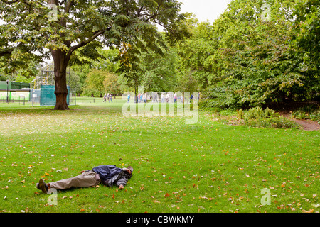 Obdachloser schlafen im St. James Park, London, England, während Menschen Ballspiele im Hintergrund spielen. Stockfoto