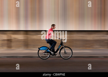 Mann auf einem Barclays Mietfahrrad Reiten mit Geschwindigkeit vor einem farbigen Hintergrund. Stockfoto