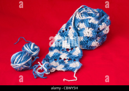 Ball der Garne und stricken Spieße. Blaue und weiße Farbe Schal auf rotem Grund Stockfoto