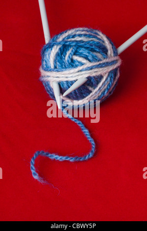 Ball der Garne und stricken Spieße. Blaue und weiße Farbenkugeln auf rotem Grund Stockfoto