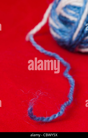 Ball der Garne und stricken Spieße. Blaue und weiße Farbenkugeln auf rotem Grund Stockfoto