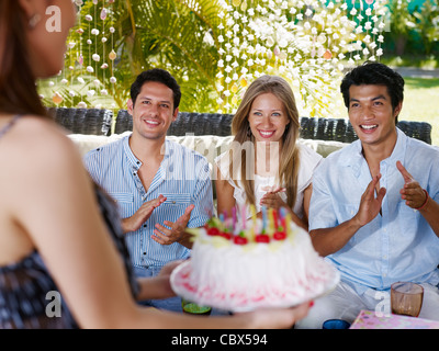 Geburtstagsfeier mit Kuchen, Getränken und glücklich kaukasischen und asiatischen Freunde Händeklatschen. Vorderansicht Stockfoto