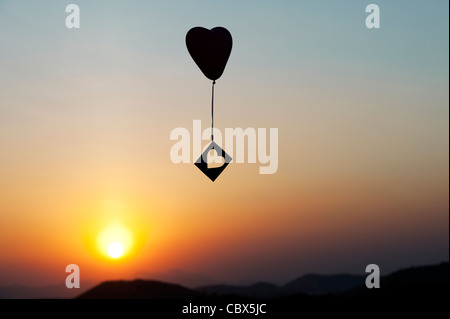 Herzballon mit Ausschneiden Herzform treiben in einem Sonnenuntergang Himmel. Silhouette Stockfoto