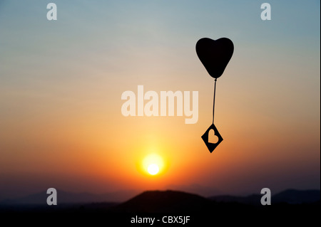 Herzballon mit Ausschneiden Herzform treiben in einem Sonnenuntergang Himmel. Silhouette Stockfoto