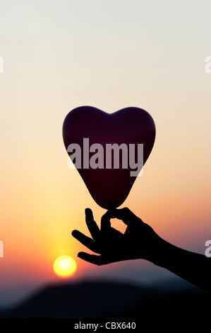 Hand mit Herz Form Ballon Silhouette gegen Sonnenuntergang Stockfoto