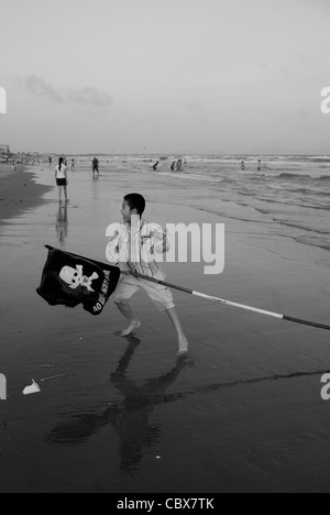 Vungtau, Vietnam. Junge, spielen am Strand mit einer Flagge für Warnungen verwendet wie die Anwesenheit von Haien oder gefährliche Strömungen. Stockfoto