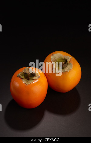 Zwei frisch geerntete Kaki, Stilleben auf schwarz Stockfoto