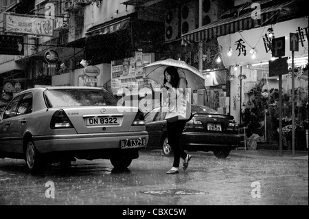 Kowloon, Hong Kong. Frau über die Straße bei starken Regenfällen. Stockfoto