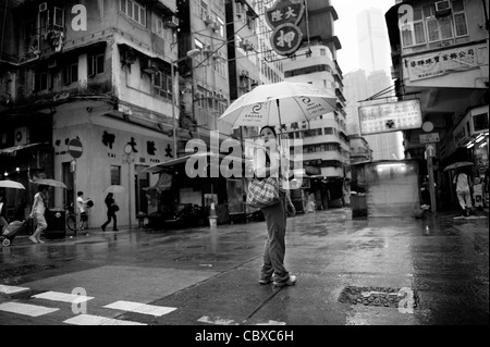 Kowloon, Hong Kong. Frau über die Straße bei starken Regenfällen. Stockfoto