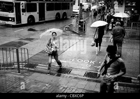 Kowloon, Hong Kong. Frau über die Straße bei starken Regenfällen. Stockfoto