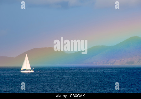 US JUNGFERNINSELN, Vereinigte Staaten – Ein Segelboot fährt in der Nähe des Fußes eines pulsierenden Regenbogens auf den US Jungferninseln. Diese faszinierende Szene zeigt das Zusammenspiel von tropischem Wetter und maritimer Aktivität, die für den karibischen Archipel charakteristisch ist, und hebt die natürliche Schönheit und die Segelmöglichkeiten in diesen Gewässern hervor. Stockfoto