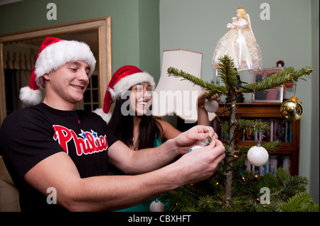 Junges Paar tragen Santa Hüte dekorieren Weihnachtsbaum, UK Stockfoto