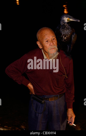 Rauchen chinesische Fischer mit einer ausgebildeten Kormoran auf der Schulter in der Nacht auf dem Li-Fluss in Yangshuo Peoples Republic Of China Stockfoto