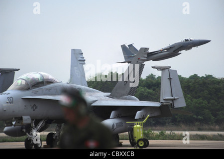 Ein F-15-Adler, der dem 44. Expeditionskämpfer-Geschwader auf der Kadena Air Base, Japan, zugewiesen wurde, hebt am 23. März 2011 von der Korat Royal Air Force Base, Thailand, hinter einem geparkten F/A-18-Hornet ab, das dem Marine All-Weather Fighter Attack Squadron 533 auf der Marine Corps Air Station Iwakuni, Japan, zugewiesen wurde. Der Eagle flog eine Übungsmission, die Teil von Cope Tiger 2011 war, die vom 14. Bis 25. März läuft. Zu den Teilnehmern von Cope Tiger gehören die US Air Force, das U.S. Marine Corps, die Royal Thai Air Force, die Royal Thai Army und die Republic of Singapore Air Force. Stockfoto