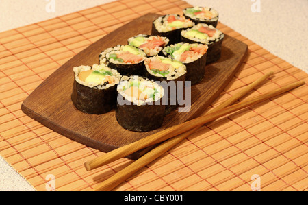 Brauner Reis Sushi-Rollen auf einer Holzplatte mit Stäbchen auf einer Bambusmatte. Stockfoto
