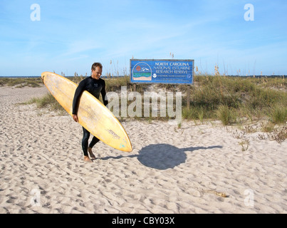 Wrightsville Beach, Wilmington, North Carolina, North Carolina. Eine Surfer geht es vorbei an einem Hinweisschild. Stockfoto