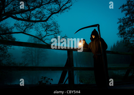 Mann sieht aus wie der Tod mit Sense auf alte Brücke Stockfoto