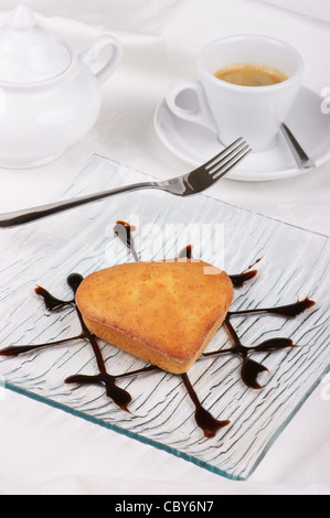 Kleinen herzförmigen Kuchen und Kaffee. Auf einer Glasschale dekoriert mit Schokoladenglasur wird Kuchen serviert. Stockfoto