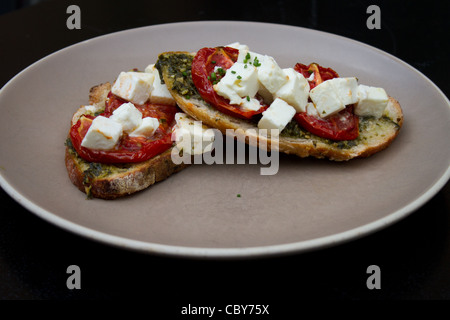 Warm gerösteten Bruschetta mit Topping aus frische und getrocknete Tomaten, Feta und geriebenen Basilikum Blätter. Stockfoto