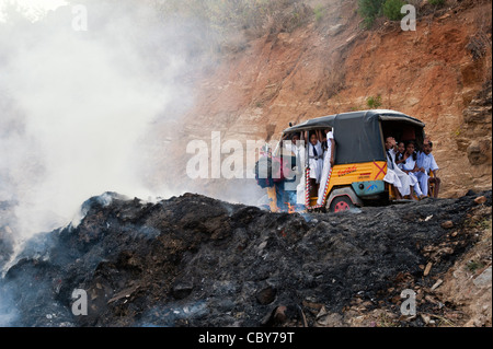 Indische Kinder in Rikscha vorbei Haushalt Abfälle am Straßenrand verbrannt wird. Andhra Pradesh, Indien Stockfoto