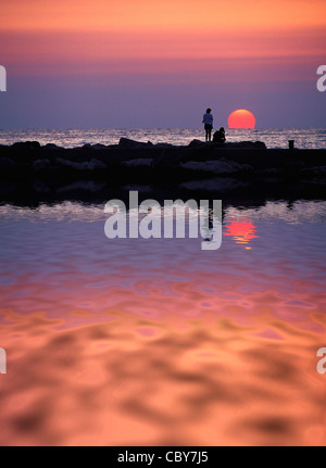 Zwei Frauen auf Wellenbrecher Silhouette gegen See Michigan Sonnenuntergang in Holland, Michigan, USA Stockfoto