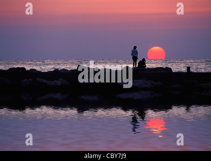 Zwei Frauen auf Wellenbrecher Silhouette gegen See Michigan Sonnenuntergang in Holland, Michigan, USA Stockfoto