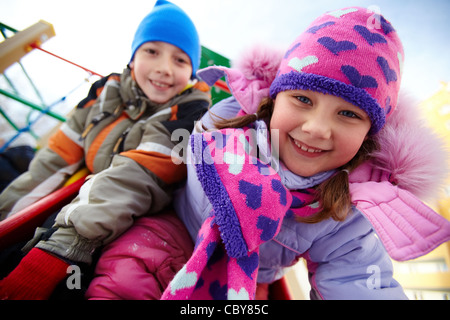 Glückliches Mädchen in Winterwear spielen im Freien mit ihrer Freundin auf Hintergrund Stockfoto