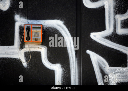 Orange Telefonzelle an einer Graffitiwand Stockfoto