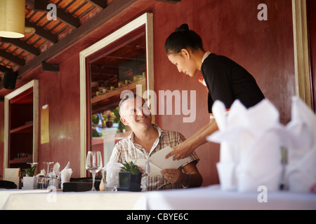 Attraktive junge asiatische Frau arbeitet als Kellnerin im exklusiven Restaurant und Teilnahme an Kunden mit Menü Stockfoto