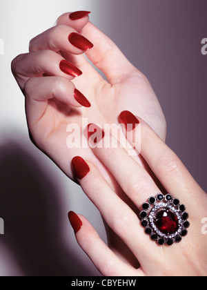 Lizenz erhältlich unter MaximImages.com Großaufnahme von Frauenhänden mit glänzendem rotem nagellack und rotem Steinring Stockfoto
