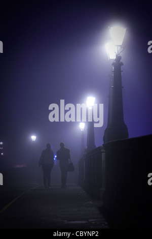 Zwei Frauen, zu Fuß über Kingston Brücke von Hampton Wick an einem nebligen Abend, tief im Gespräch. Stockfoto