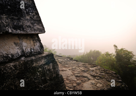 Auf der linken Seite ist Teil des oberen Teils Tempel IV, die höchste von den Pyramiden in Tikal. Auf der rechten Seite des Rahmens beleuchtet die aufgehende Sonne Nebel über dem Kronendach des Dschungels. Stockfoto