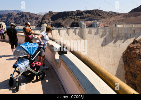 Hoover Dam Tourist Viewing Platform Nevada | HOOVER DAM, Nevada – Touristen lehnen sich über ein geschwungenes Geländer auf der Aussichtsplattform des Staudamms, um den Bogen der Betonwand und des Lake Mead dahinter zu genießen. Der 1936 fertiggestellte Hoover Dam erhebt sich 726 ft (221 m) über dem Colorado River und ist ein National Historic Landmark, das die Grenze zwischen Nevada und Arizona überspannt. Seine Einlasstürme und die hier sichtbare niedrige Wasserlinie spiegeln den jahrzehntelangen Trockendruck auf den Stausee wider. Stockfoto
