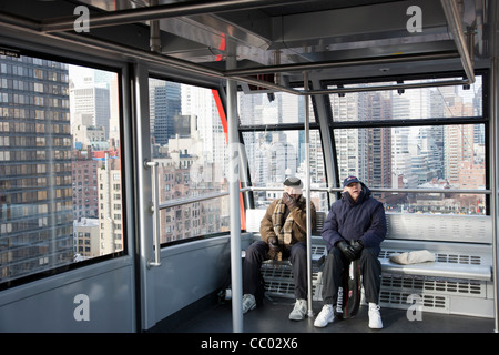 Zwei Passagiere an Bord geleitet die Roosevelt Island Tram für Roosevelt Island, mit der East Side von Manhattan im Hintergrund Stockfoto