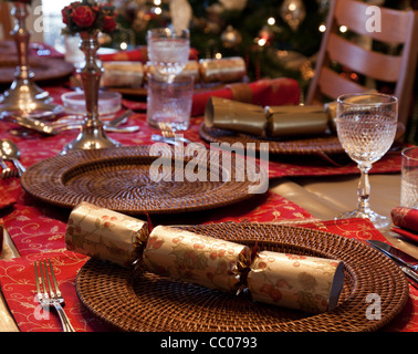 Christmas Cracker am Tisch für Weihnachtsessen mit Kerzen und Baum im Hintergrund Stockfoto