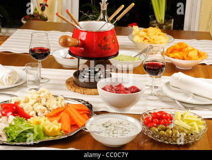 Tabelle mit Fondue-Topf, Gemüse, Fleisch, Saucen und Wein Stockfoto