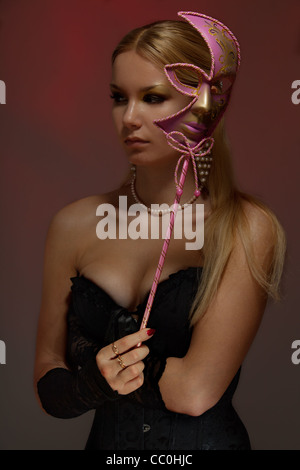 Ruhig wunderschöne junge Frau an Maskerade hält Rosa venezianischen Maske Stockfoto