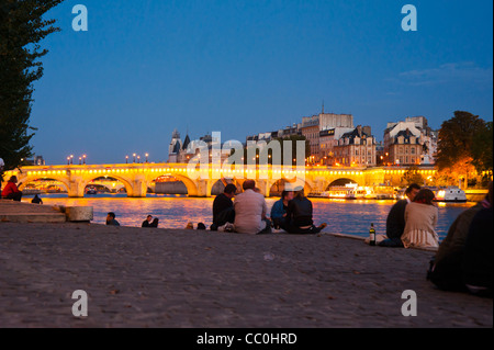 Paris, Frankreich, Gruppenmitglieder sitzen von hinten, genießen die seine-Quay in der Abenddämmerung, mit Panoramablick auf die Pont Neuf-Brücke hinten, Nachtlichter Stockfoto