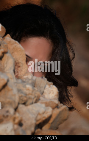 Ernste junge Frau versteckt sich hinter Felsen Stockfoto